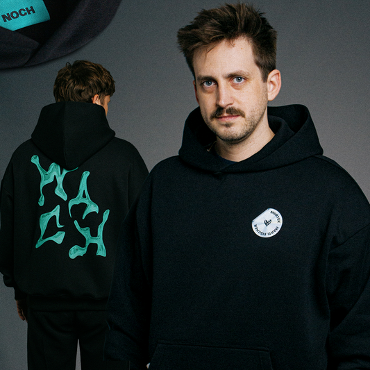 Zweifach-Komposition: Im Vordergrund eine Person in einem schwarzen Hoodie mit dem silbernen Sticker „MIRRTEK MARTI FISCHER“ auf der Brust; im Hintergrund eine zweite Person mit dem Rücken zur Kamera, auf dessen Hoodie der grüne „WACH“-Rückendruck zu sehen ist. Oben links ist zusätzlich ein Detailbild des Etiketts mit der Aufschrift „NOCH“ eingeblendet.